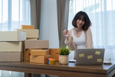 Excited asian young entrepreneur waving fists, got good new orders on digital laptop while working at home. small business owner concept.の写真素材