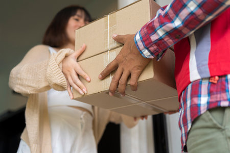 Delivery mail man giving parcel box to recipient,young owner accepting of cardboard boxes package from post shipment,home courier and delivery service mind concept.Cargo carrier holds a cardboard boxの写真素材