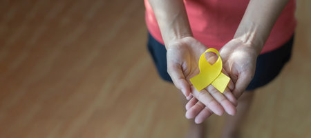 Adult hands holding yellow gold ribbon, sarcoma awareness, bone cancer, cancer awareness. Woman holding yellow ribbon, closeup. cancer awareness concept.の写真素材