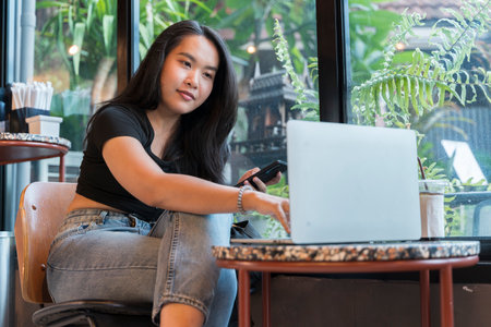 Young asian beautiful woman using smart phone and laptop for business, online shopping, transfer money, financial, internet banking. in coffee shop cafeの写真素材