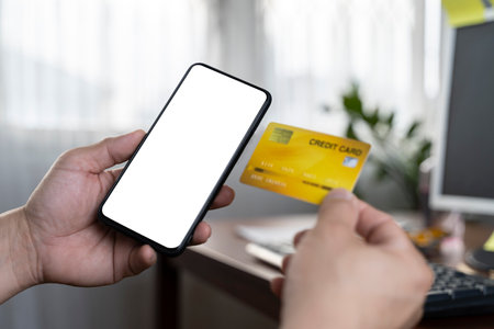 Hand holding credit card and using smartphone. Businessman or entrepreneur working from home. Online shopping, e-commerce, internet banking, spending money, work from home concept.の写真素材