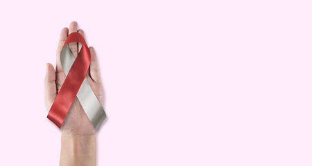 Head and neck cancer awareness with burgundy ivory white color ribbon on hand support background, bow color for Oral Squamous Cell Carcinoma, Throat, Laryngeal and Pharyngeal Cancerの写真素材