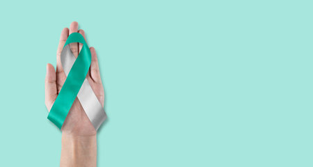 Teal and white ribbon for cervical cancer awareness month in January and HPV prevention with bow on hand supportの写真素材