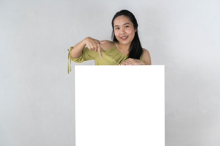 Young attractive asian woman showing and holding blank white board, Showing empty board for input your text. White banner in hand blank presentation gray backgroundの写真素材