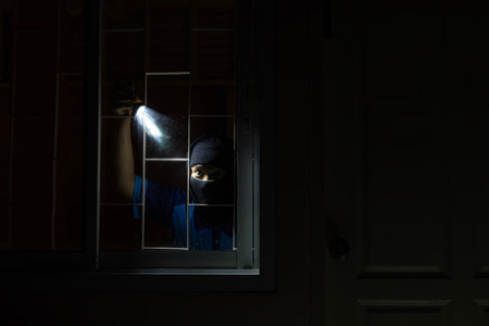 Burglar breaking in to home in night through window. Burglar at night with flashlight at window of the house. Thief Breaking House Window To Enter Houseの写真素材