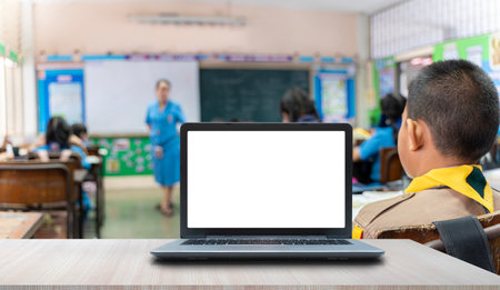 Background image of opened laptop with blank white screen on teachers desk in school auditorium, copy space. Teacher female speaker giving presentation for students in classroomの写真素材