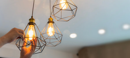 An electrician is installing spotlights on the ceiling. Handyman choosing between energy save and cheap incandescent lamp while changing light in the appartmentの写真素材