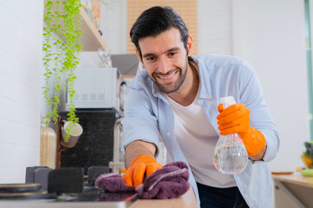 Clean your cares away. a young man disinfecting a kitchen counter at home. Young handsome man with apron and protective gloves wiping sink and faucet in kitchen.の写真素材