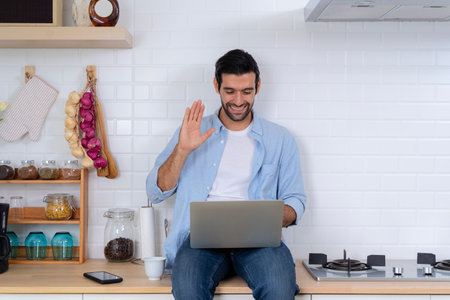 Handsome man using a laptop pc in the kitchen, calling online indoor, business webinar training, studying online. Gain new knowledge via video conferencing. Self-education, e-learning conceptの写真素材