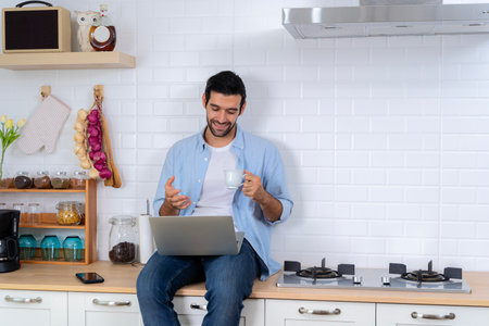 Gain new knowledge via video conferencing. Self-education, e-learning concept. Handsome man using a laptop pc in the kitchen, calling online indoor, business webinar training, studying online.の写真素材