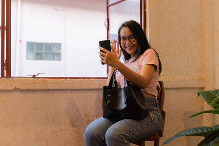 Smiling young woman during online video call. Online meeting with friends. Portrait of young smiling student girl make video call from smartphone to her best friend, having break, telling good news.の写真素材
