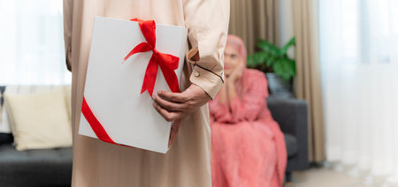 Muslim Husband Giving Wrapped Gift Box To Surprised Wife Celebrating Christmas Holiday Or Valentines Day Together Sitting On Couch At Home. Holiday celebrations, gifts and presentsの写真素材
