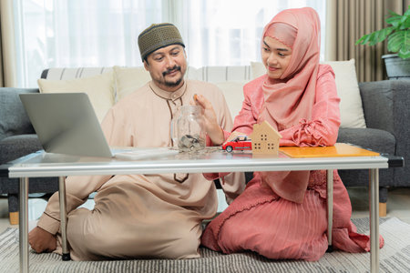 Muslim couple with jar of coins. Woman hand putting money in the glass jar labeled held by a man, save and investment money for prepare in the future. Saving money to buy house, car, life insuranceの写真素材