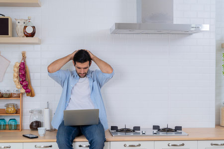 Serious business man working at home having problem with job thinking to solve problem. Handsome man using a laptop pc in the kitchen, concentrate and thinking with him job.の写真素材
