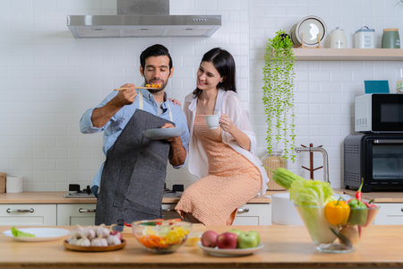 The man who was inhaling the smell of breakfast being made with his girlfriend nearby. Couple in love having fun while preparing a breakfast together on a beautiful morning.の写真素材