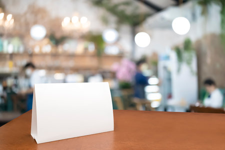 Blank menu frame label mockup. Mock up menu frame on table in bar restaurant, stand for booklet with white sheet of acrylic tent card paper in blur cafeteria, cook chef in background.の写真素材