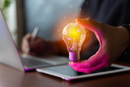 Accounting concepts and creativity. Businessman holding glowing lightbulb on wooden table with laptop computer as business solution and creative marketing idea concept.の写真素材