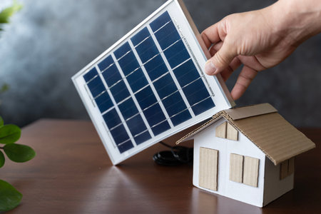 Close up view of alternative energy engineer pointing at solar panels for future energy in studio. Small cardboard house and solar panels close upの写真素材