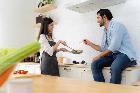 The man was tasting the food his girlfriend made for breakfast. A young couple in love having fun while preparing a breakfast together on a beautiful morning. Cooking, together, kitchen, relationship.の写真素材