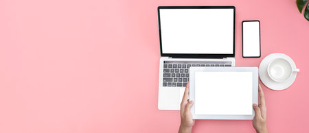 Pastel pink office desk top view cup of coffee, woman hands using laptop, smartphone and holding tablet screen, blank space for advertising, panoramic image style.の写真素材