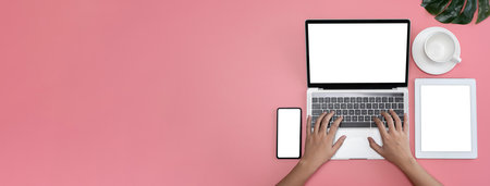 Pastel pink office desk top view cup of coffee woman hands using laptop, smart phone and tablet blank screen empty space for media advertising panoramic view styleの写真素材