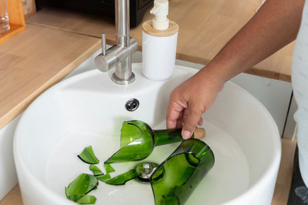 Broken green glass bottle inside white sink in modern kitchen.Broken glass bottle looks dangerous. recycling waste setの写真素材
