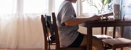 Smiling young asian teenage girl in eyeglasses typing on laptop computer at home office sitting at desk. Female independent professional student enjoying studying online using notebook pc.の写真素材