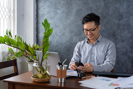 Confident smiling businessman using smartphone in a home office. Checking new e-mails. Businessman holding smartphone sit in office working online on gadget with copy space.の写真素材