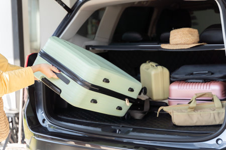 Woman loading suitcase into car trunk, preparation for trip.  Open car boot packed for family vacation. Young beautiful woman travel concept female take luggage baggage suitcase and other stuff.の写真素材