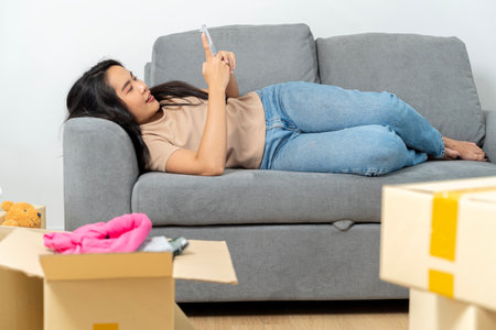 Woman using Smart phone for moving to college, leaving apartment ready for movers pick up with package of cardboard boxes for moving to a new house in banner. Moving boxes.の写真素材