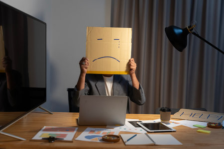 Portrait of businessman covering his face with paper mask with sad face drawn on it, bad negative sullen depression anonymouse person.の写真素材