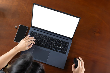 Top view of hand use laptop computer with blank screens on white office desk table.Cropped shot of businesswoman is working on computer with isolated white display for your advertising text message.の写真素材