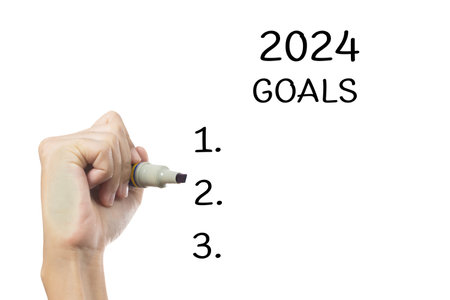 A  person writing their goals for 2024 on a glass whiteboard. They are using a marker to write, and they have already written down a few goals and they.の写真素材