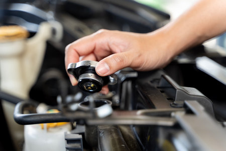 A person is holding a funnel and pouring coolant into the radiator of a car and they are standing in front of a car. The hood of the car is open, and the radiator cap is removed.の写真素材