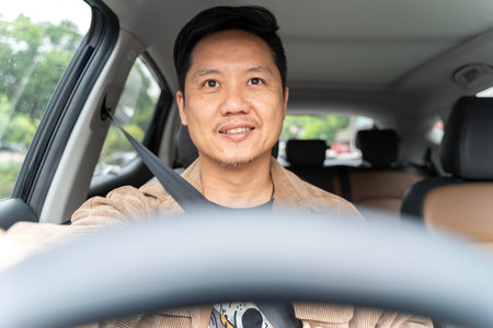 A man is driving a car and smiling. He is wearing a brown jacket and a tie. The car is parked in a parking lotの写真素材