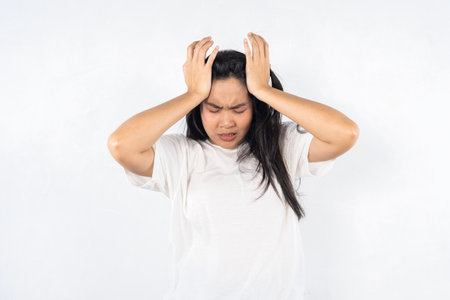 A woman with her hands on her head, looking very upset. She is wearing a white shirtの写真素材