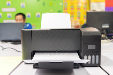 A black printer is open and has a white sheet of paper inside. The printer is on a desk in front of...
