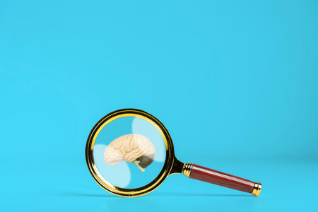 Magnifying glass and human brain on blue background, mental health care concept. A magnifying glass is held up to a brain.の写真素材