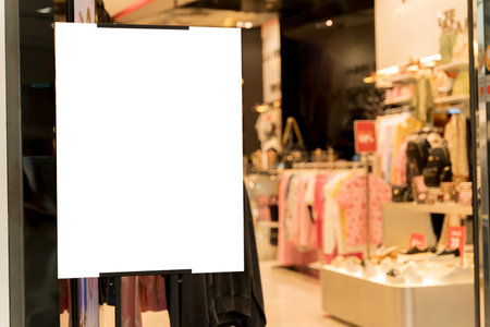 Blank poster frame with clothing store background. Mockup blank billboard on the wall of casual clothes shop. White billboard in brightly lit clothing store mockup photography. Racks of apparel.の写真素材