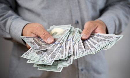 Close up of man hand holding 100 dollar bills currency. Close-up of American dollars in hands, counting banknotes, light background. Concept of finance, business, income.の写真素材