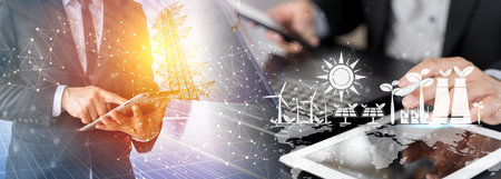 A focused businessman analyzes renewable energy designs on his laptop with holographic blueprints, in an office overlooking wind turbines. Energy efficient chart on a house model in the office.の写真素材