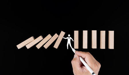 Planning Risk and Strategy in Business, Image of hand Businessman stopping and protection for collapse of wooden block game being falling down dominoes effect problem solving of prevent.の写真素材
