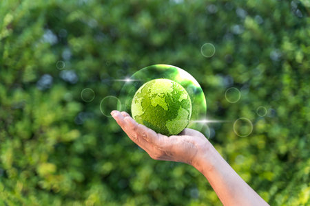 Hand holding a green grass earth globe in bubble with light reflection, flare light on natural background for Friendly globe day, environmental management, business concept.Banner.Copy space.の写真素材