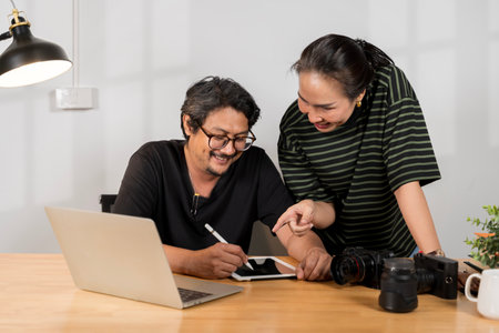 Asian young friendly pretty success female photographer sit smile hold and point camera screen in hands try to check choose best. Photographer and designer working together at home office.の写真素材