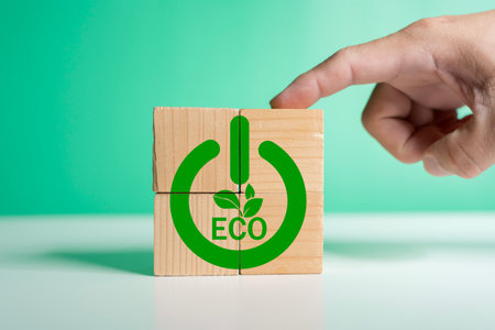 A finger presses eco power button symbol on wooden blocks with green leaves icon, representing...
