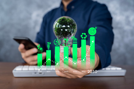 Hand holding light bulb with tree inside and green timeline growth chart. Concept for sustainable energy, environmental development, eco innovation, clean technology, and future green business planningの写真素材