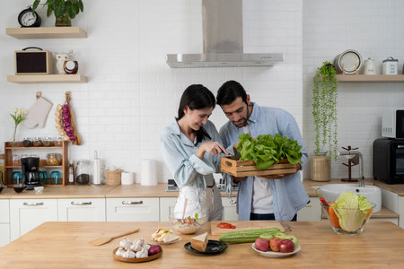 Young couple cooking healthy food together at home, selecting fresh green lettuce for salad preparation. Natural ingredients, happy lifestyle, and teamwork in modern kitchen atmosphere.の写真素材