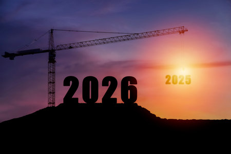 Silhouette of construction crane lifting 2025 number with 2026 standing on the hill during sunset. Concept of progress, time transition, planning, development, and new year vision and strategy.の写真素材