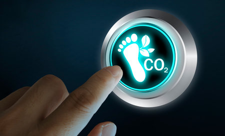 Close-up of human finger pressing illuminated button with carbon footprint and CO2 icon. Concept of climate change, sustainability, environmental awareness, and carbon emission reduction technology.の写真素材