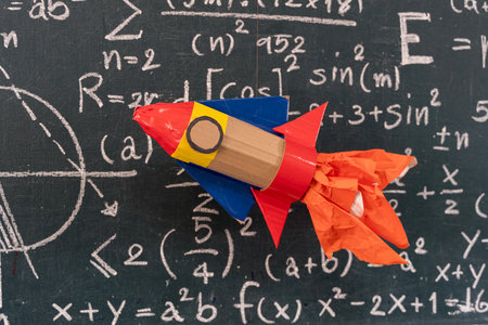 Handmade paper rocket model in front of chalkboard with mathematical formulas, representing creativity, education, learning, imagination, science, technology, and innovative ideas for students and children.の写真素材